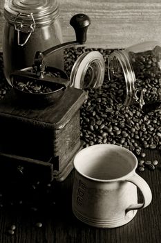 Photo of roasted coffee beans, coffee cup, antique grinder on a wooden table.
