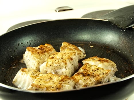 Someone frying seasoned white fish in a frying pan