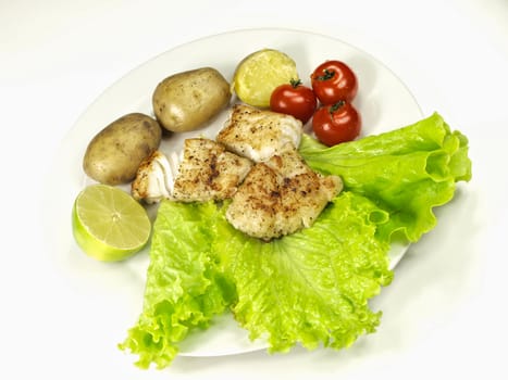 Fried white fish on a plate, with potatoes, salad, lime and tomatoes