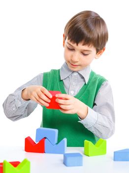 A smiling little boy is building a toy block. Isolated on white background