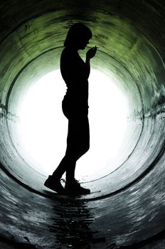 Silhouette of a young girl smoking in sewer pipe