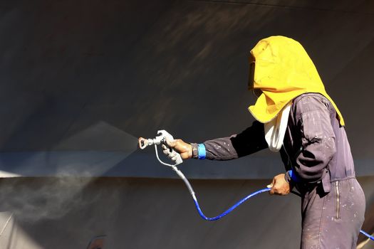 worker painting ship hull using airbrush