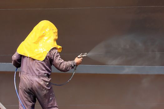 worker painting ship hull using airbrush