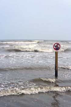 A no swimming sign at the beach with rough surf 