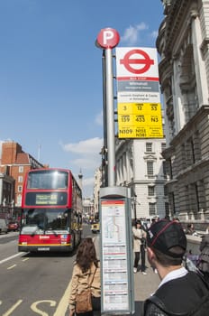 LONDON, UK - APRIL 02: Bus stop with red double-decker bus approaching and commuters waiting. April 02, 2012 in London.