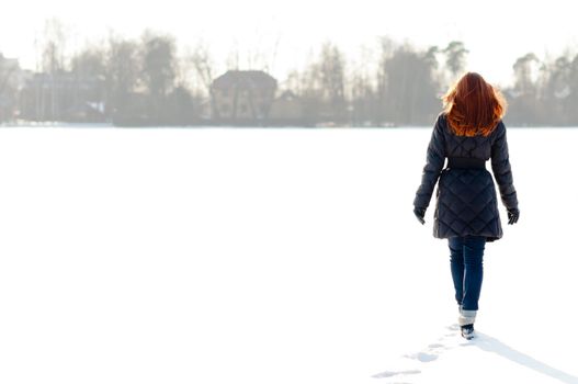 Pretty red haired girl walking on frozen lake and making footpath