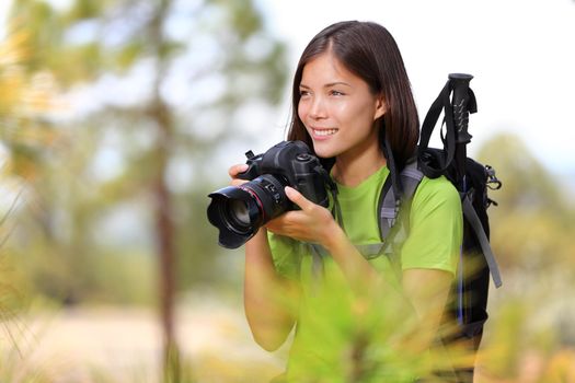 Nature travel photographer woman taking pictures in forest during hiking trip. Beautiful happy smiling young woman holding professional SLR camera. Mixed race Chinese Asian / Caucasian girl photographing