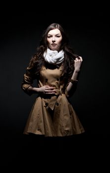Expressive fashion studio shot of young and beautiful woman wearing brown overcoat on dark background. (Professional makeup and hair style).