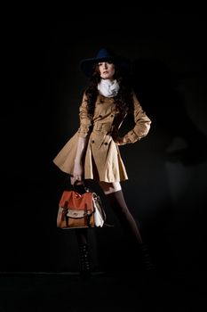 Expressive fashion studio shot of young and beautiful woman wearing brown overcoat on dark background. (Professional makeup and hair style).