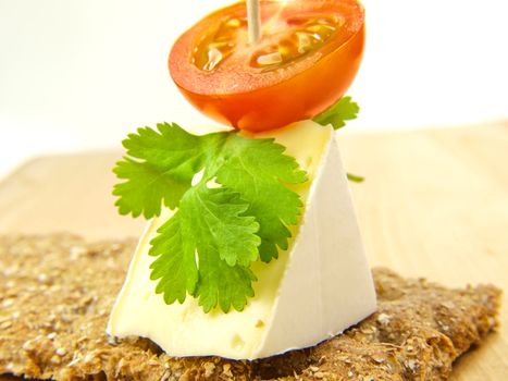 Cracker on wooden board, with soft cheese and tomato