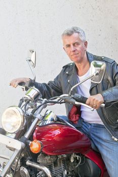 Portrait of a Caucasian motor biker in casual attire and tight lipped looking into lens sat on a red cruiser. Generic shot location was Bombay India