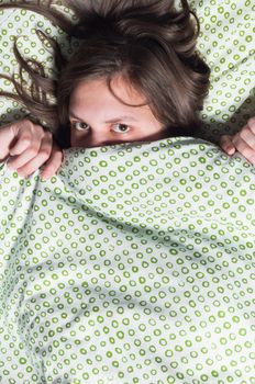 Portrait of a young girl hiding under blanket