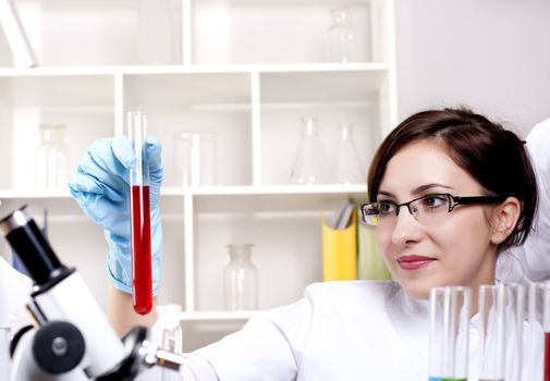 portrait of a beautiful woman chemist, looks at a test tube with red fluid