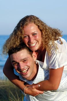 A happy woman and man in love at beach. The young man is carrying his girlfriend on the back of his shoulders.