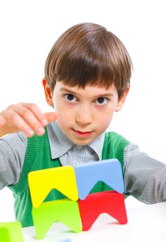 A smiling little boy is building a toy block. Isolated on white background