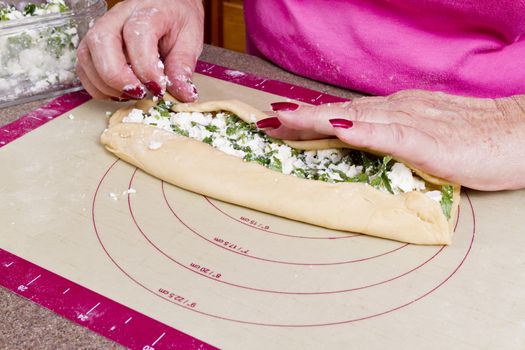 Older lady hands are wrapping Turkish feta cheese Pide pockets.