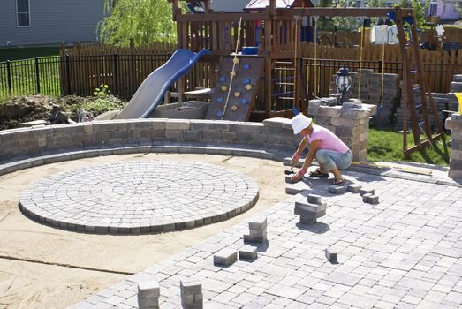 Woman with the white hat paving patio at the backyard of their house.