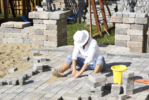 Woman with the white hat paving patio under the sun.