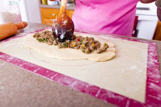 Well used wooden utensil putting ground beef on to dough to make Turkish Pide pocket.