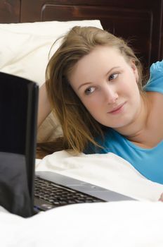 Pretty girl lying on the bed and looks at laptop