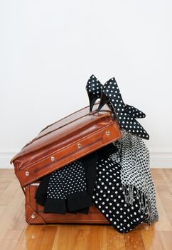 Black and white polka dot clothes and shoes in a vintage leather suitcase.