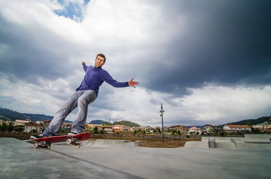 Skateboarder on a grind with dark clouds background at the local skatepark.