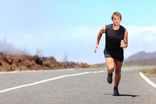 Man running / sprinting on road in mountains. Fit male fitness runner during outdoor workout. Young caucasian man.