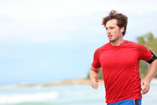 Man jogging on beach. Male runner running listening to music on mp3 player or smart phone. Young caucasian male fitness sport model in red t-shirt.
