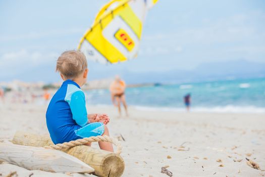 Back view cute 2 years old boy looking at kiting on tropical beach