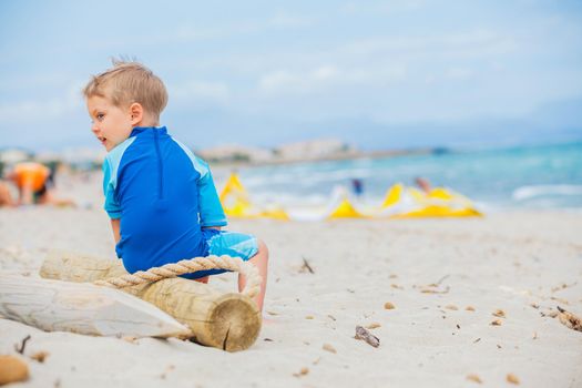 Back view cute 2 years old boy looking at kiting on tropical beach