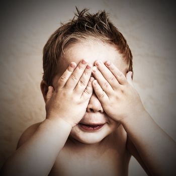 Portrait of little boy closed eyes with his hands, studio shot