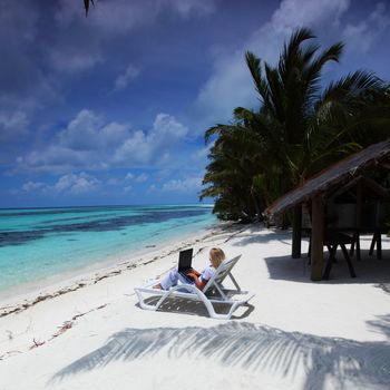 business woman with laptop lying on a chaise lounge in the tropical ocean coast