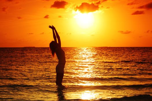 happy woman standing on a sunset in ocean waves