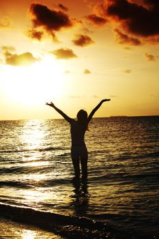 happy woman standing on a sunset in ocean waves