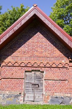 Rural farm building of red brick with wooden doors locked with padlock.