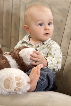 The child with amazed face is sitting on a couch and playing with teddy bear