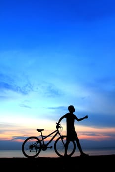 Silhouette of man riding bicycle with beautiful lake near by at sunset