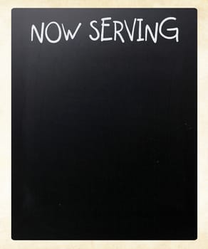 "Now serving" handwritten with white chalk on a blackboard