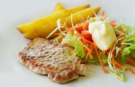 Grilled pork steak served with chips, potatoes and vegetables