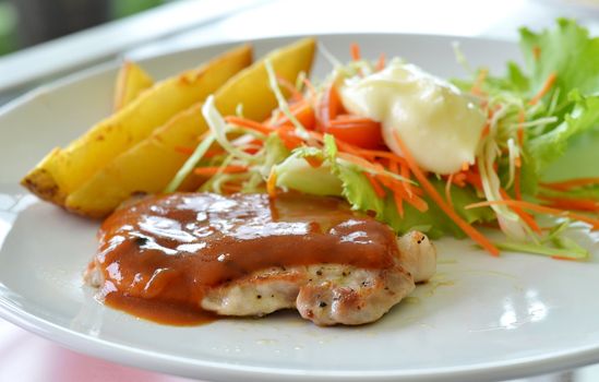 Grilled pork steak served with  tomato sauce, potatoes and vegetables ,