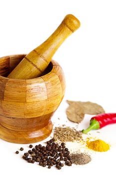 Mortar with pestle and variety of spices over white