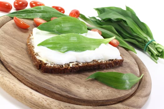 Slice of bread with cottage cheese, ramson and chopped tomatoes on a light background