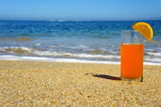 A glass of Orange Juice standing in the sand.
