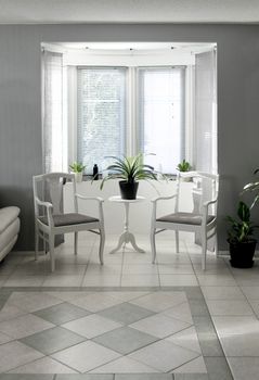 Bright bay window interior with classic chairs and table on tiled floor 