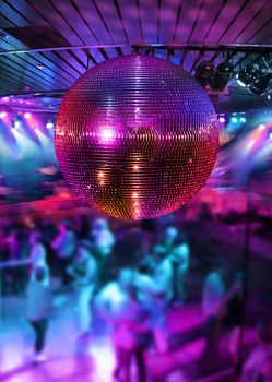 People dancing under colorful lights of disco mirror ball