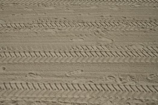 Footprints and tyre tracks in sand heading forward, seen above