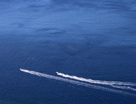 Two speeed boats leaving a white trail on blue sea