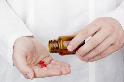 Close-up photograph of a hand pouring red tablets out of a transparent bottle into another hand.