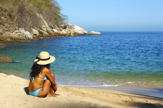 Young woman sitting at the beach looking over the ocean. 
