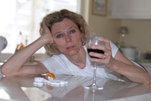 mature addictet woman drinking wine and pills